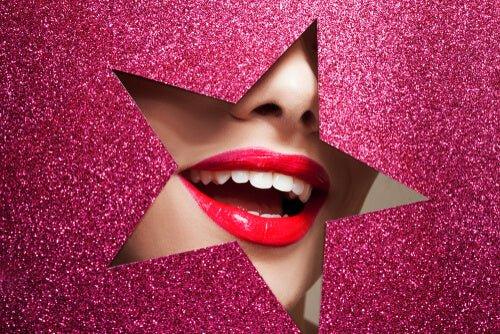 Close-up of a woman's bright white smile with glossy red lips, framed by a glittery pink star cutout background — symbolizing modern cosmetic dentistry and glamorous smile trends.