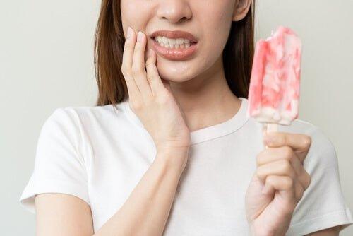 Woman experiencing tooth sensitivity while holding a red popsicle, indicating discomfort from cold food or drink