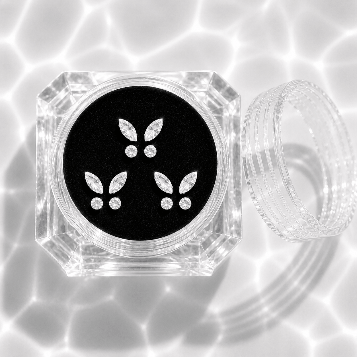 Three sets of clear crystal butterfly tooth gems in a transparent acrylic display case