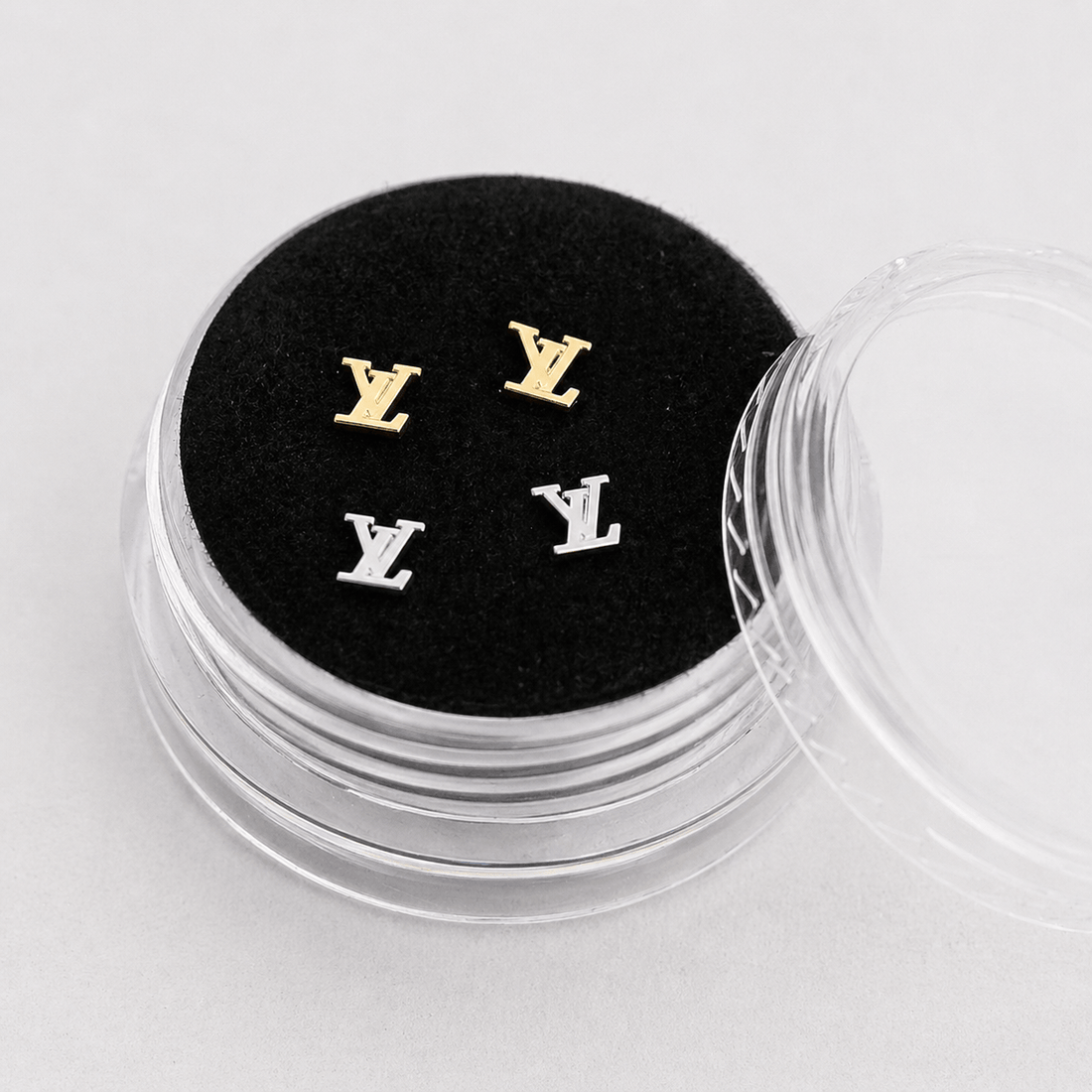 Gold and silver LV logo tooth gems displayed in a clear acrylic box with black velvet insert for premium product presentation