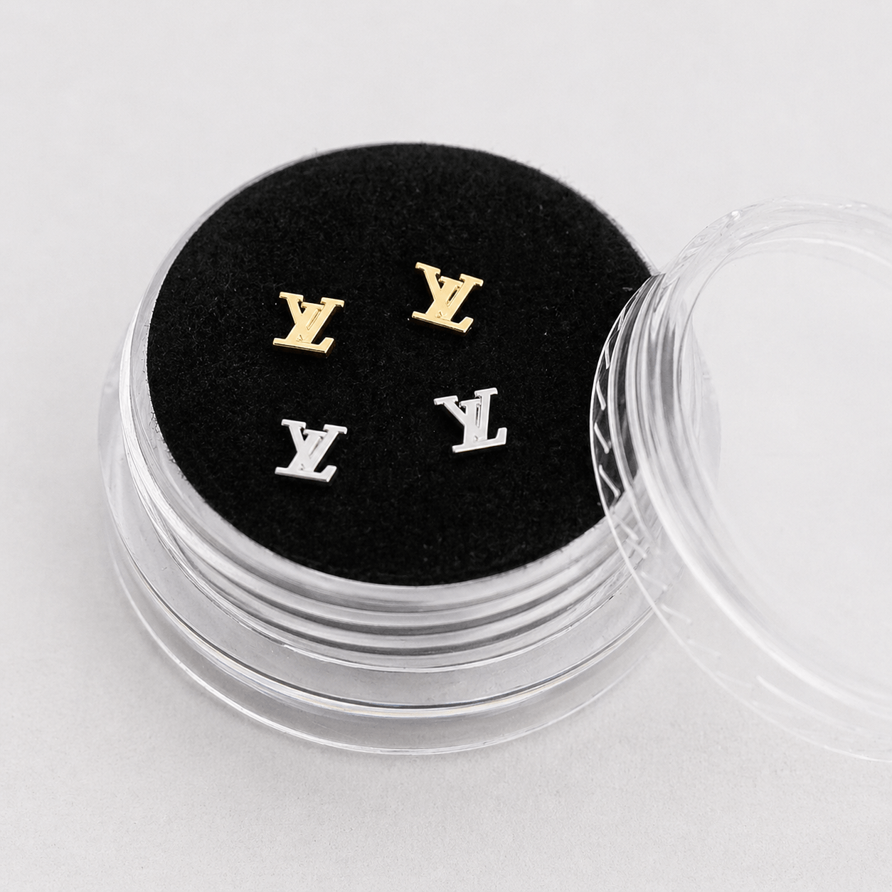 Gold and silver LV logo tooth gems displayed in a clear acrylic box with black velvet insert for premium product presentation