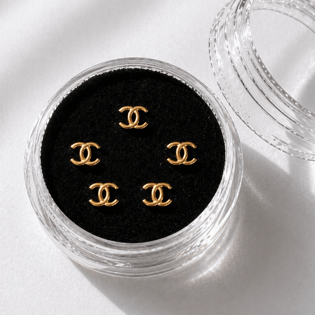 Gold Chanel-inspired tooth gems 5-pack displayed in a clear acrylic case with black velvet insert for luxury smile jewelry.