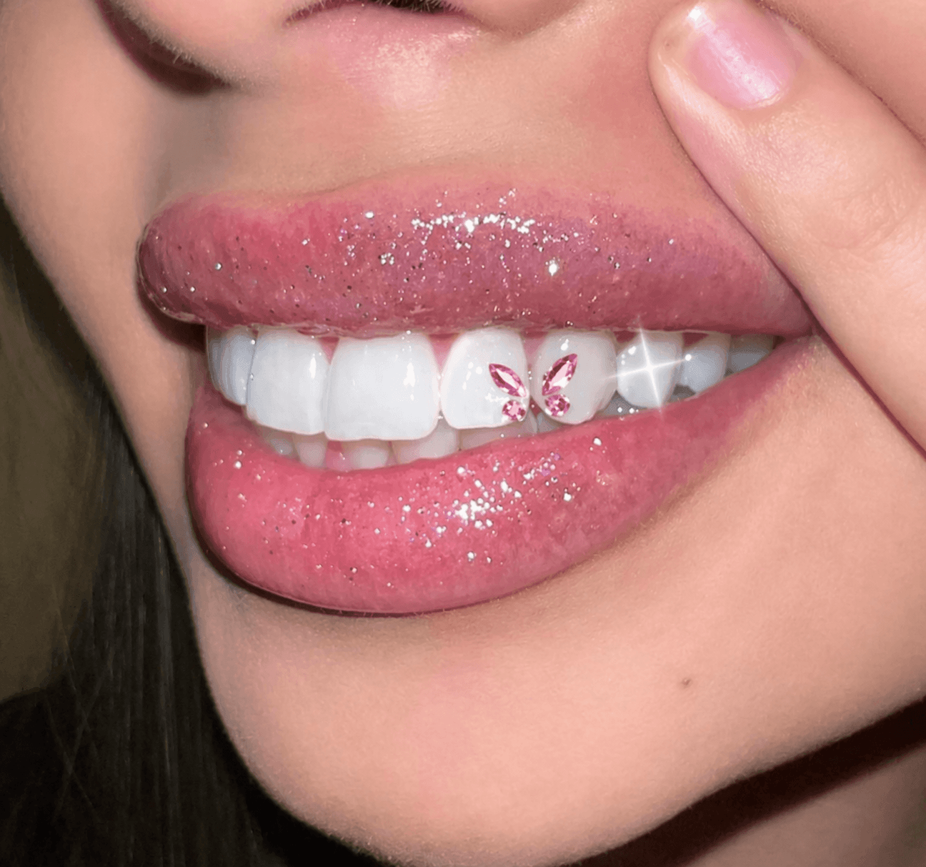 Close-up smile with a pink butterfly tooth gem on a front tooth and glossy lips.