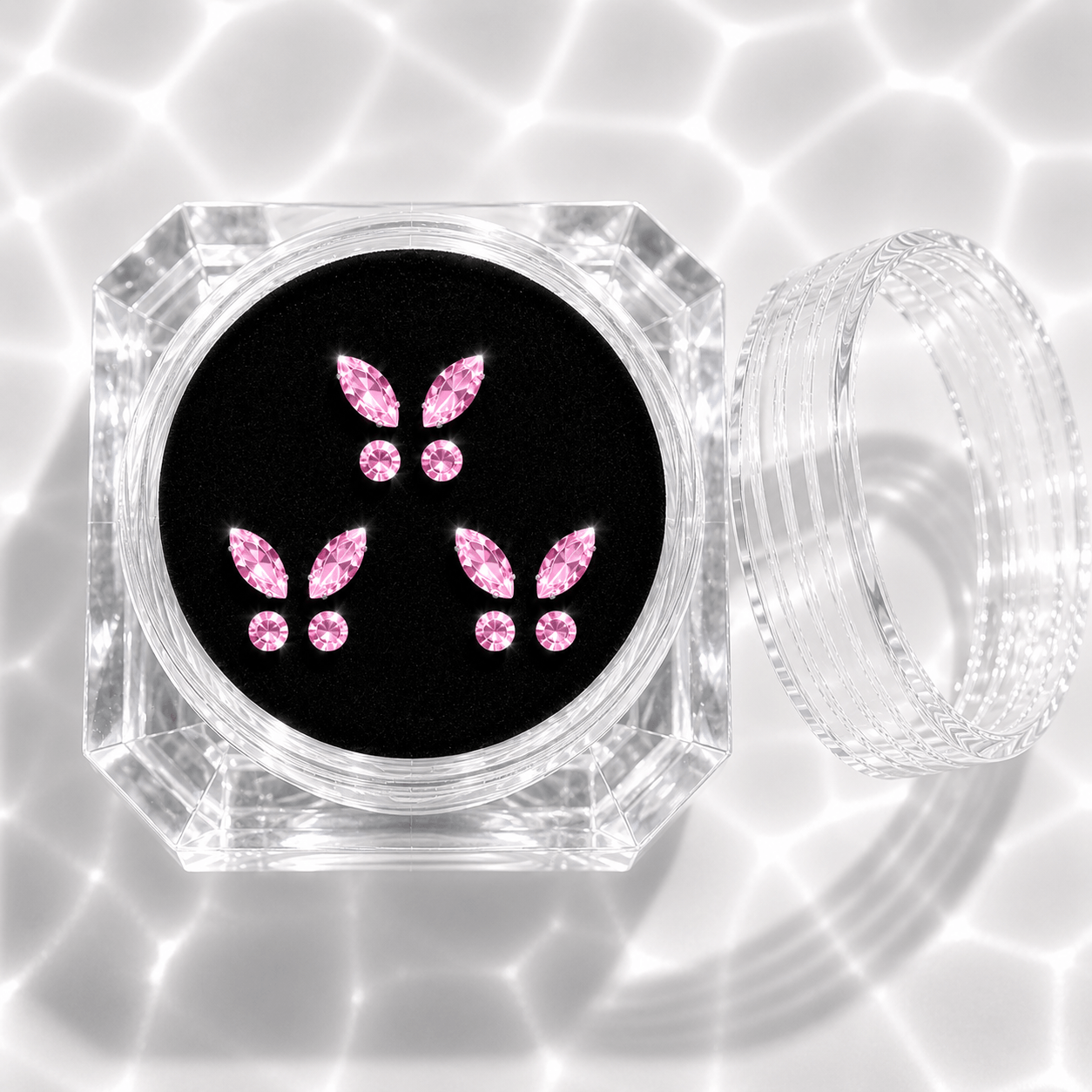 Three sets of pink crystal butterfly tooth gems in a transparent acrylic display case