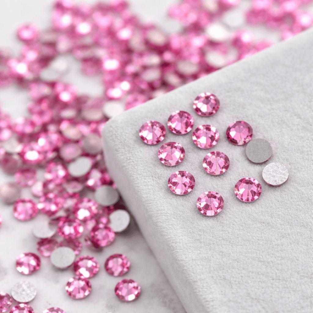Pink crystal tooth gems displayed on a soft gray velvet surface with matching loose gems in the background