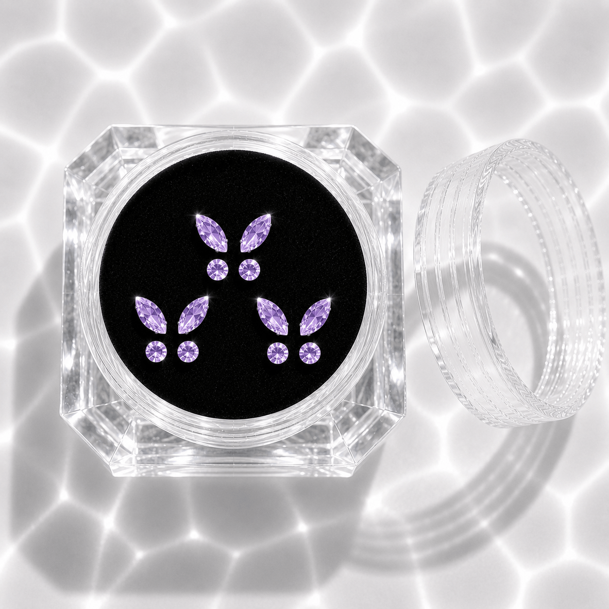 Three sets of purple crystal butterfly tooth gems in a transparent acrylic display case