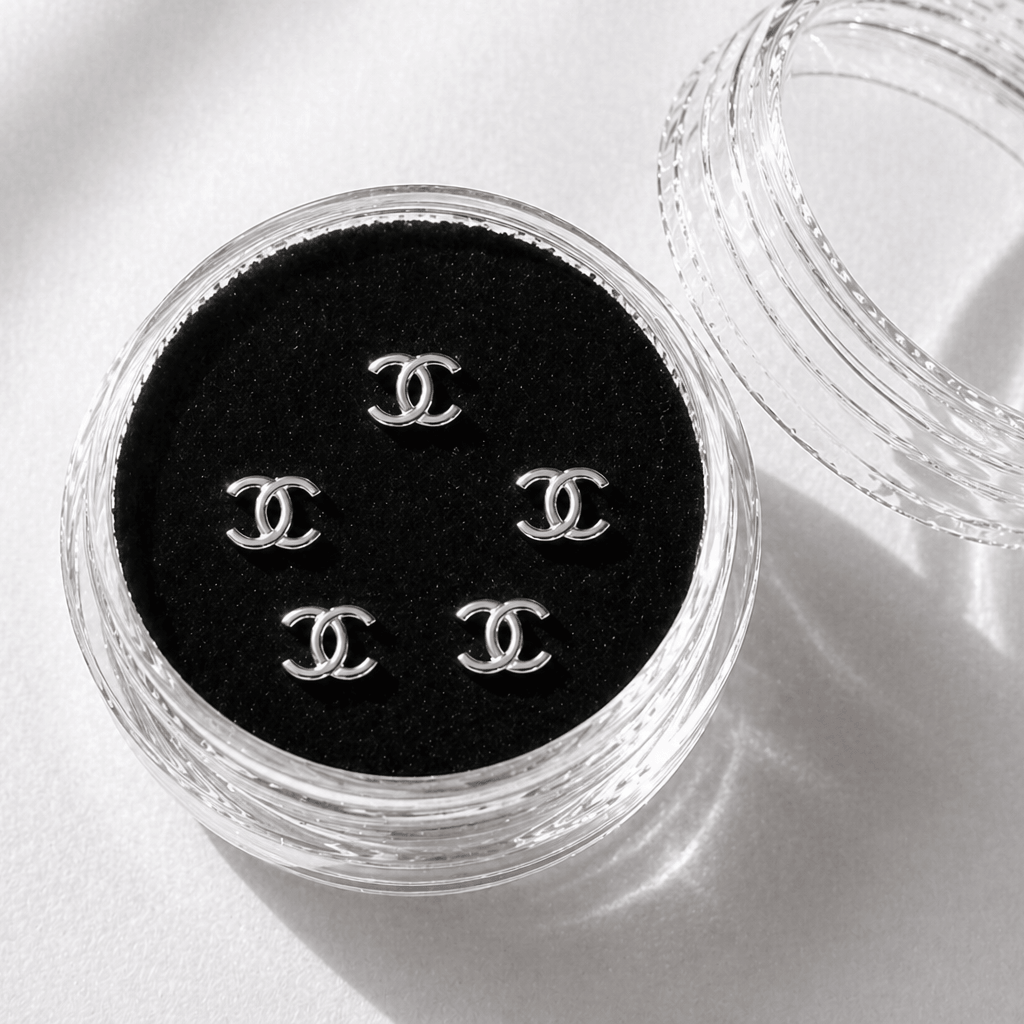 Silver Chanel-inspired tooth gems 5-pack displayed in a clear acrylic case with black velvet insert for luxury smile jewelry.