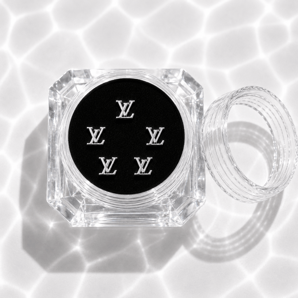 Five silver LV-style monogram tooth gem charms in a clear acrylic display case